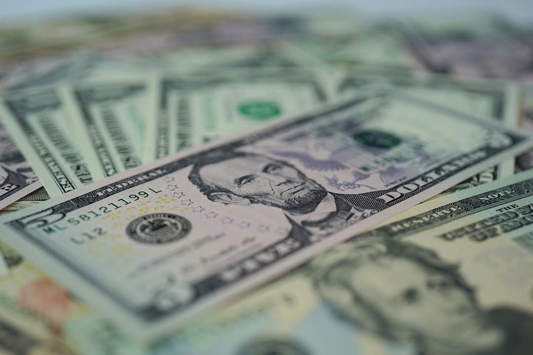 Banknoty dolarowe i moneta z symbolem dolara na tle gotówki – po podwyżce stóp Fed złoto traci na wartości.