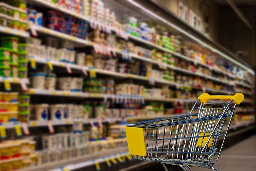 Wózek sklepowy w alejce supermarketu między półkami z nabiałem i artykułami spożywczymi, symbol rosnących cen w USA